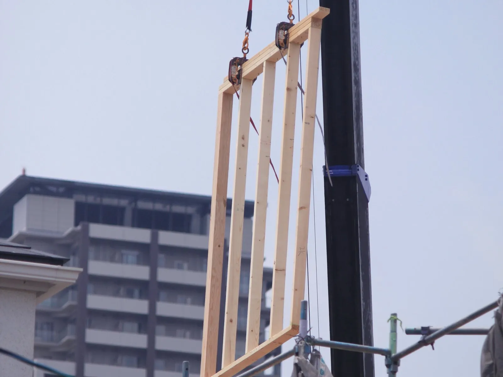 クレーンで壁パネルを吊り上げる建て方の現場